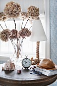 Vintage alarm clock, dried hydrangea flowers and table lamp on side table