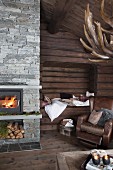 Cosy living area with brown leather armchair in front of alcove in log wall and fire in fireplace