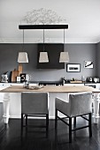 Chairs with pale grey upholstery around wooden table below modern pendant lamps in elegant kitchen