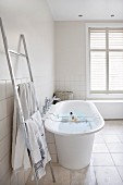 Free-standing bathtub with bath caddy and stainless steel ladder-style towel rail in modern bathroom