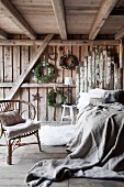 Schlafzimmer in rustikalem Holzhaus, Rattanstuhl neben Bett mit Leinen-Überwurf, an Kopfende Upcycling Holzbretter