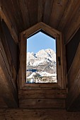 View of Dolomite Mountains through rustic dormer window of chalet