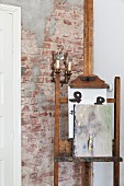 Painting on old easel in front of antique sconce lamp on unrendered brick wall