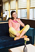 Brünette Frau in pfirsichfarbenem Pulli und gelber Hose auf Sofa in altmodischem Café
