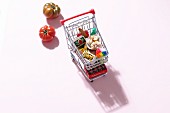 A mini shopping trolley filled with toy foodstuffs next to fresh tomatoes