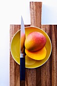 A halved mango on a plate with a knife