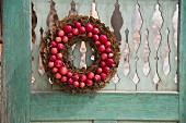 Wreath of bark and small red apples hung on weathered wooden door