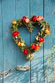 Heart-shaped wreath of multicoloured ranunculus on blue-painted wooden wall