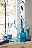 Various clear and blue glass bottles and twigs in front of window