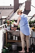 Frau bepflanzt Tontöpfe an Pflanztisch auf Dachterrasse