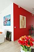 Red and orange tulips in front of male nude artwork on red-painted accent wall in modern interior