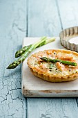 Asparagus and smoked salmon tartlets with asparagus spears on white chopping board