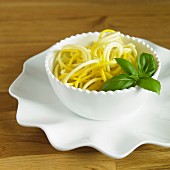 Yellow courgette spaghetti with basil in a white bowl