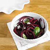 Vegetable spaghetti made from beetroot with Gorgonzola and basil in a white bowl