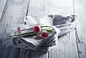 Grey linen napkin and bellis daisies tied with white ribbon on wooden surface