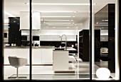 Blick durch Schaufenster in Showroom Designerküche, weisser Drehstuhl gegenüber weisser Theke in offenem Kochbereich