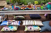 Niedriger Gartentisch, in asiatischem Stil, mit farbigen Gläsern und Blumendeko, Sitzkissen auf Holz Terrassenboden