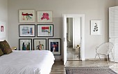 Double bed with white bedspread and gallery of artworks on wall in modern bedroom