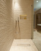 Walk-in shower in designer bathroom with natural-effect tiles; shelf niche with indirect lighting in back wall