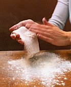 A raw fish fillet being dusted with flour