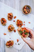 A hand holding bruschetta topped with tomatoes, basil and garlic