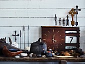 Still-life arrangement of holiday souvenirs and metal figurines on top of old clock against white wood-clad wall