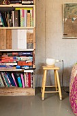 Table lamp on retro wooden stool next to bookcase made from reclaimed boards