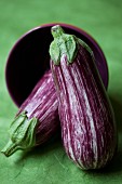 Two striped aubergines with a tipped-over bowl