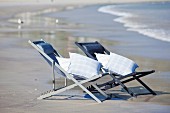 Two deckchairs with cushions on seashore