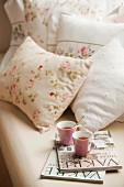 Zeitschriften und Teetassen auf Bett mit romantisch blumiger Bettwäsche