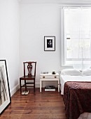 Schlicht eingerichtetes Schlafzimmer mit Holzboden, antikem Stuhl und Holztischchen als Nachttischablage