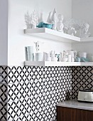 Black and white, geometric wall tiles below shelves of white crockery and ornaments