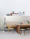 Modern dining table, wooden chair, stools and bench against half-height wall panel with elegant crockery on top