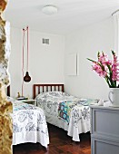 Schlichter Schlafraum mit Einzelbetten und Holzgitter als Kopfteil, im Vordergrund Blumenstrauss in Krug