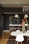 White wooden table and classic chairs in open-plan kitchen with woman at counter in background