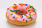 A doughnut with colourful sprinkles on a white surface