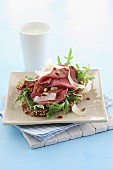 A slice of bread topped with roast beef, rocket and pine nuts