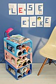 Side table with magazine compartments made from plastic drinks crates in 3 colours; pages of book on wall with letters spelling 'Reading corner' in German