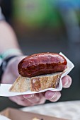 A hand holding a sausage on a slice of bread