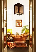 Blick durch offene Flügeltür auf freistehende Kupfer-Badewanne und Männerportrait , Accessoires in südamerikanischem Stil auf Boden