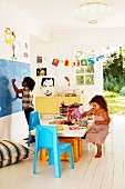 Kinder beim Spielen am Tisch und vor Schiefertafel in dekoriertem Kinderzimmer, im Hintergrund offene Tür mit Gartenblick