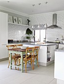 Vintage kitchen table and wooden chairs next to free-standing central island in modern, open-plan kitchen with white fronts