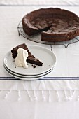 Chocolate tart, sliced, and a single slice with cream on a plate