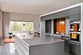 Open-plan modern kitchen in pale grey with orange accents