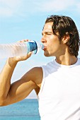 Junger sportlicher Mann trnkt Wasser aus Flasche am Meer