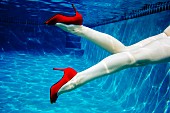 A woman's legs with red high heels underwater in a swimming pool