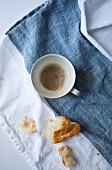 An almost empty cup of espresso and croissant crumbs on a linen cloth