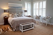 Country-house-style bedroom with bench at foot of double bed and white wicker chairs