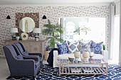 Blue and white living room with mixture of patterns on wallpaper, cushions and rug