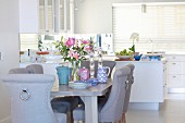 Elegant upholstered chairs, lilies and crockery on table in elegant dining area of open-plan kitchen